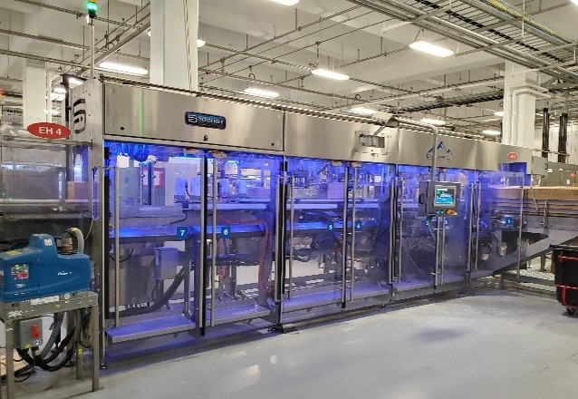 Automated packaging machinery in a factory setting, showcasing advanced technology with illuminated sections and control panels.