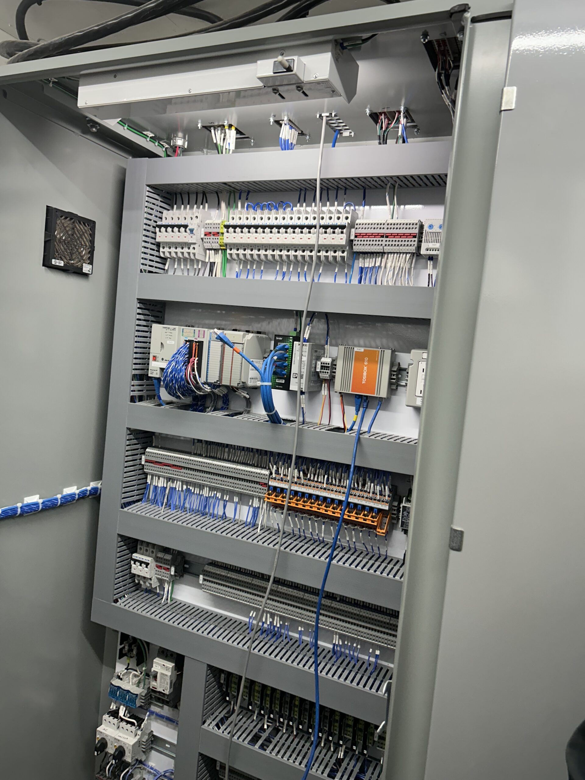 Industrial processing equipment in a clean facility, featuring a control panel, pipes, and a stainless steel tank, designed for manufacturing applications.