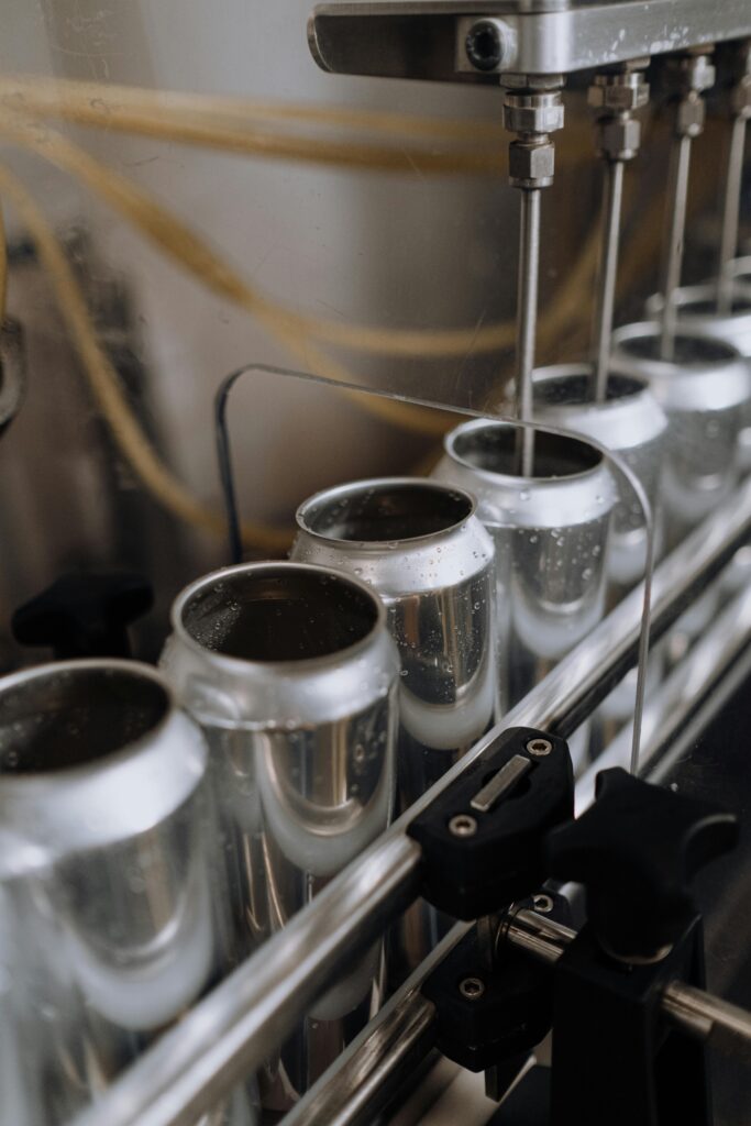 Cans being filled with liquid at a beverage production line, showcasing the machinery used in the bottling process.