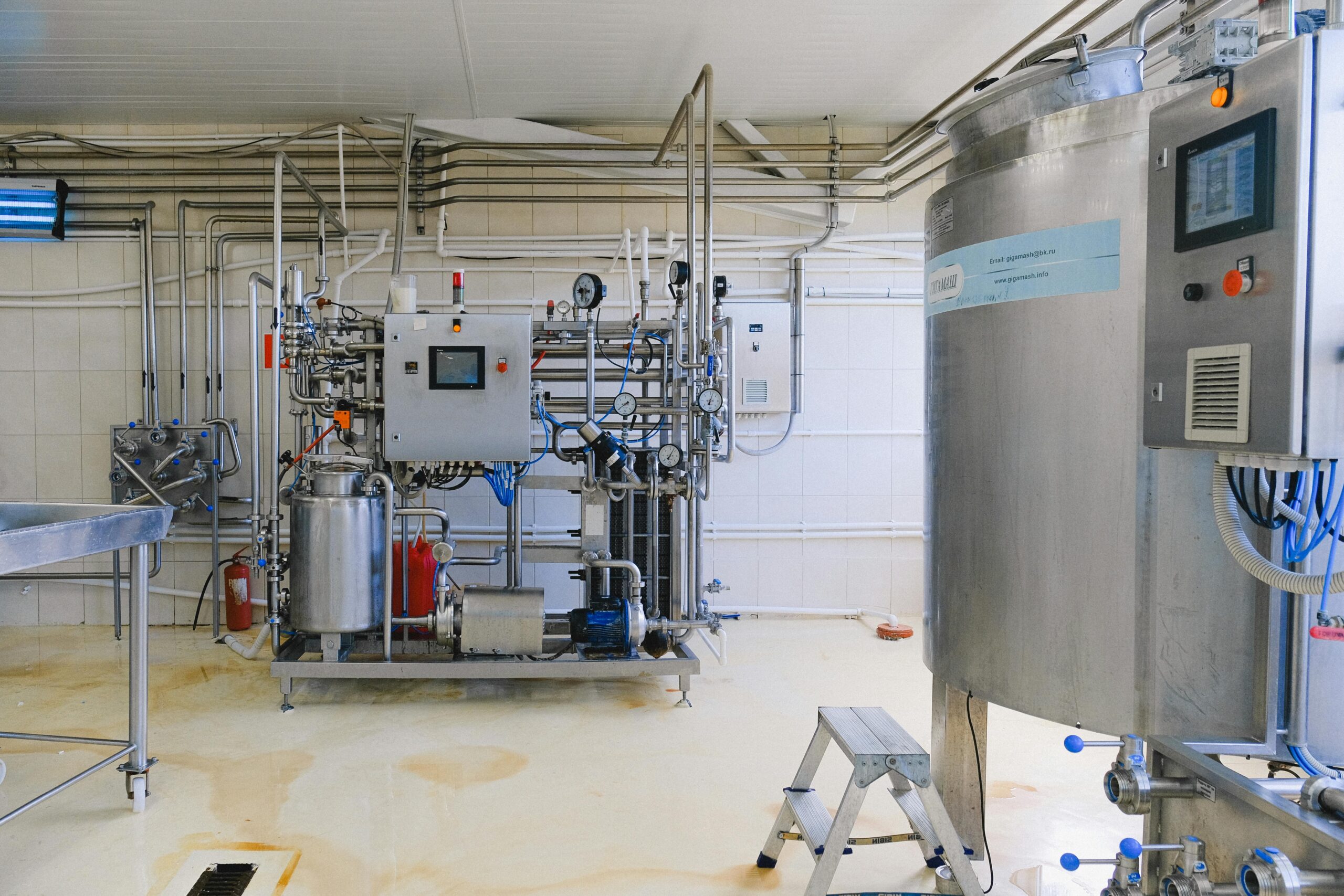 Industrial processing equipment in a clean facility, featuring a control panel, pipes, and a stainless steel tank, designed for manufacturing applications.