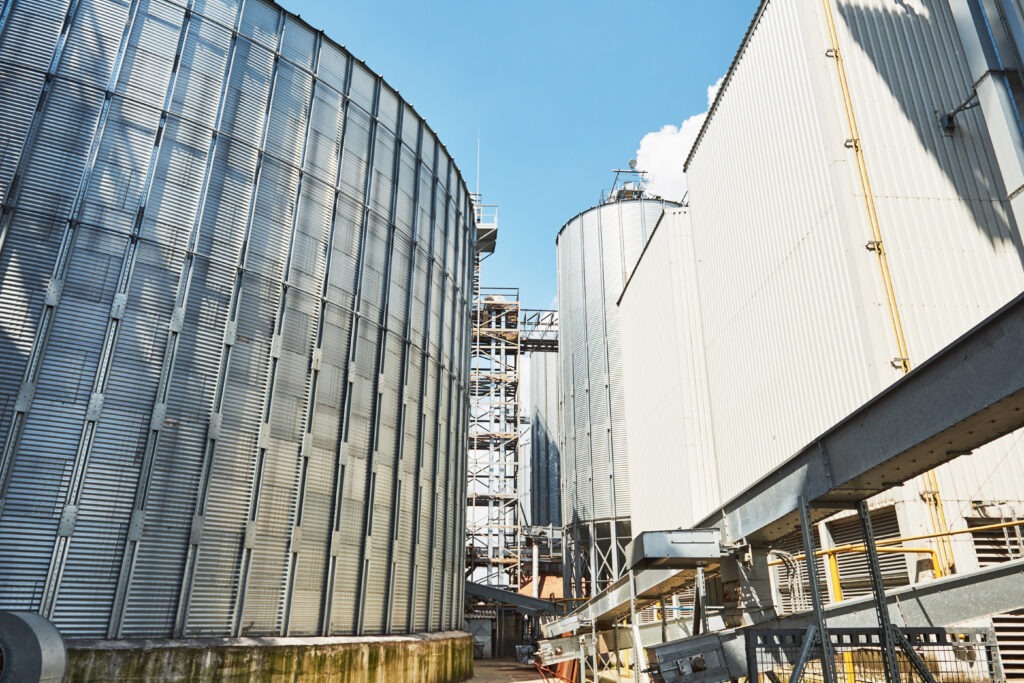 Industrial silos and storage tanks against a blue sky; metallic structures dominate the view, suggesting a modern agricultural or industrial facility.