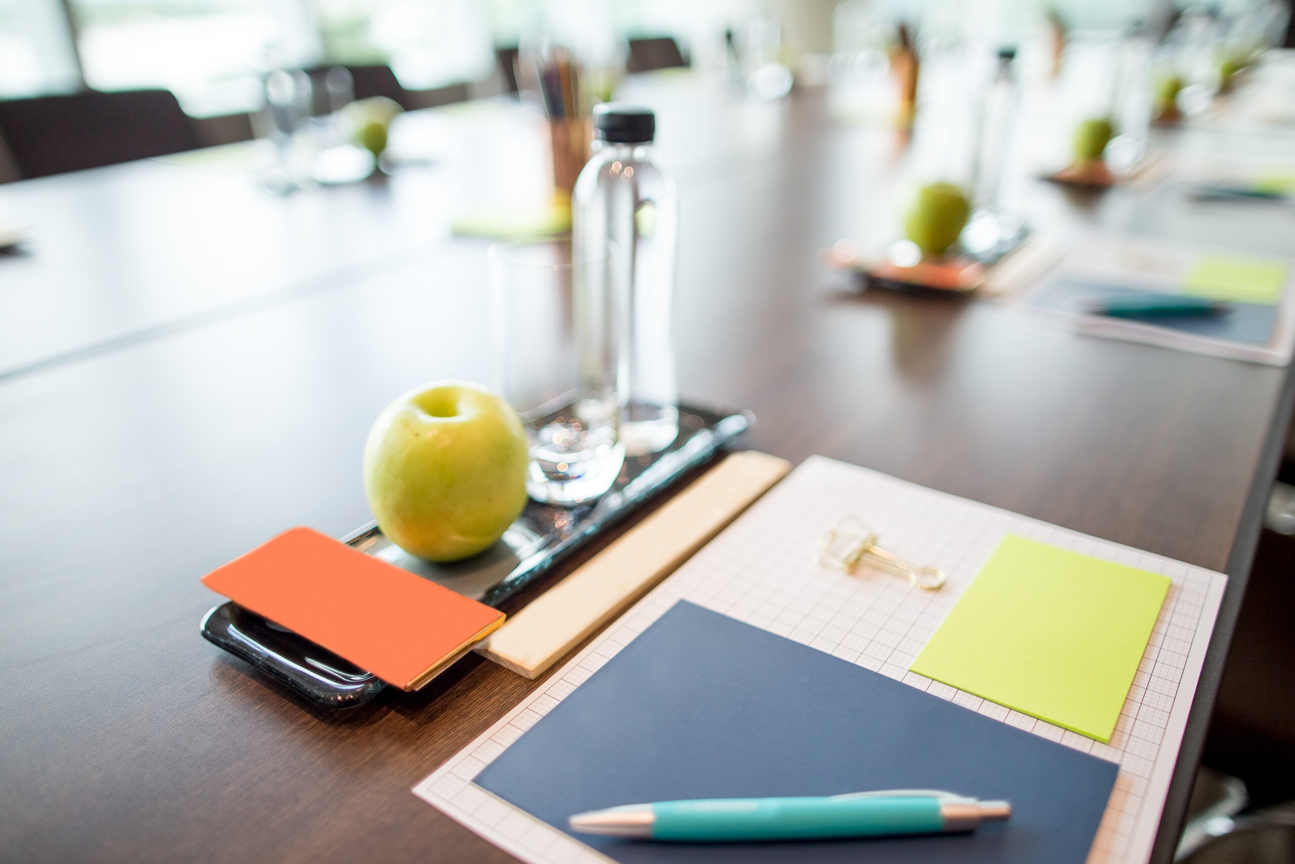 Close-up of a conference table setup with a green apple, water bottle, notepads, and a pen, creating a professional, organized atmosphere.